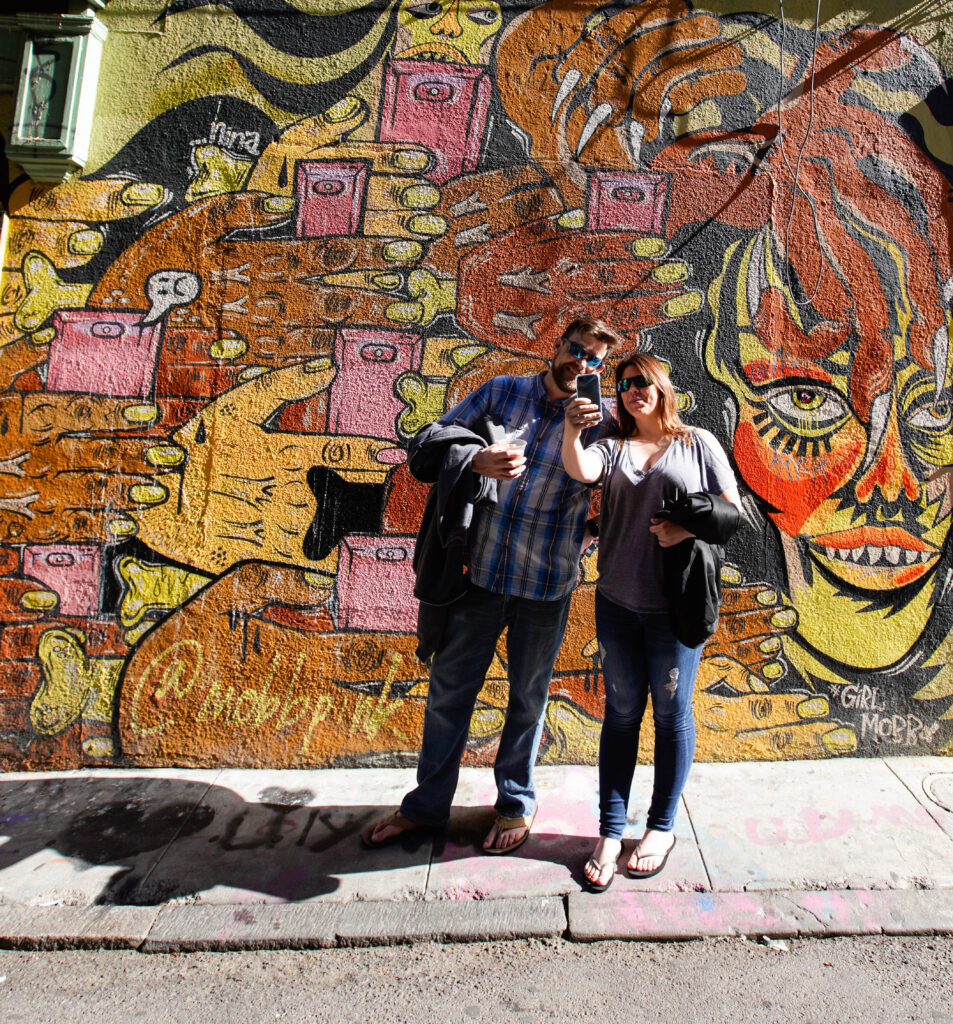 Two people taking a selfie in front of a mural on a client appreciation event in San Francisco. 