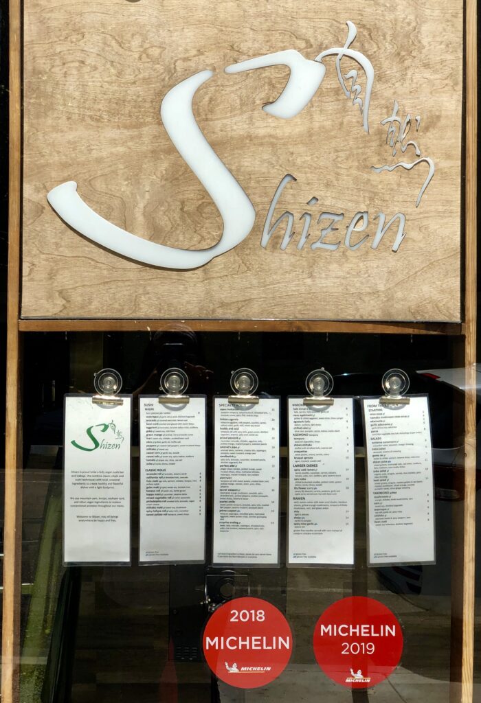 Menus displayed in the window of Shizen Vegan Sushi Bar and Izakaya, a Michelin-recommended vegan restaurant known for its sushi and ramen.